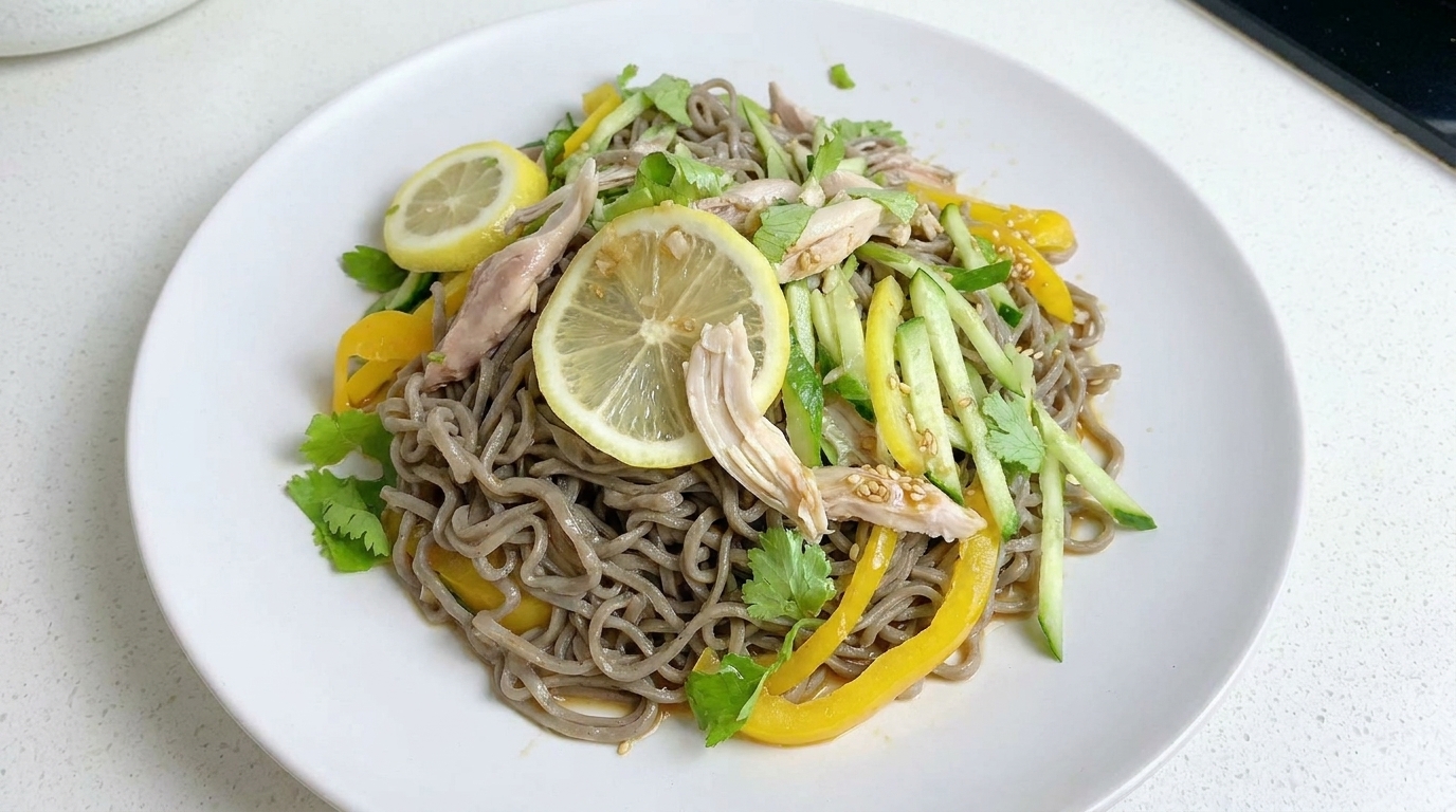 Una ensalada de fideos de trigo sarraceno ligera y cítrica, coronada con pollo desmenuzado, verduras frescas en juliana y rodajas de limón.