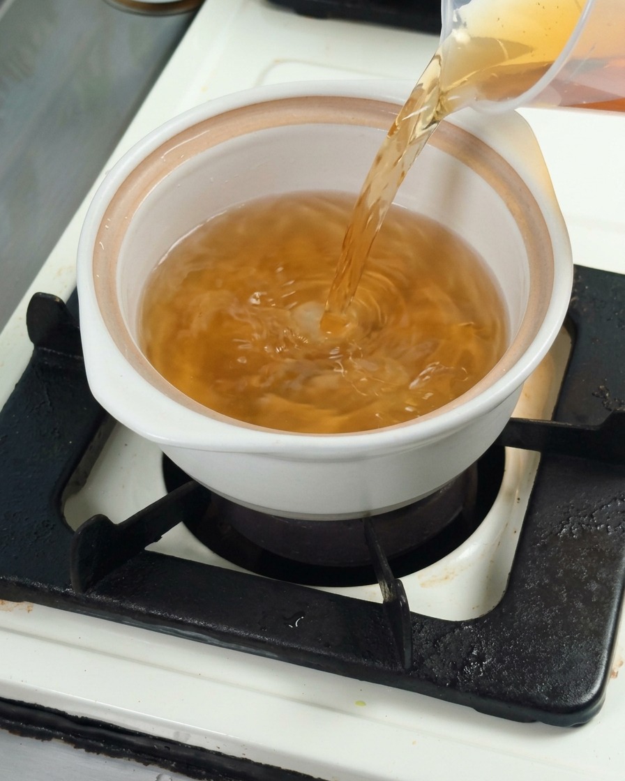 Vertiendo caldo dashi de kombu en una cazuela blanca de cerámica para preparar la base.
