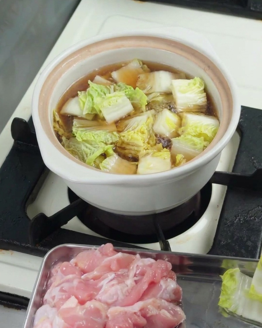 Baby bok choy cortado cociéndose a fuego lento en una olla blanca con tapa.