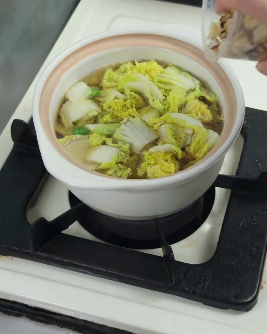 Trozos crudos de muslo de pollo añadiéndose a la olla con el bok choy y el caldo.