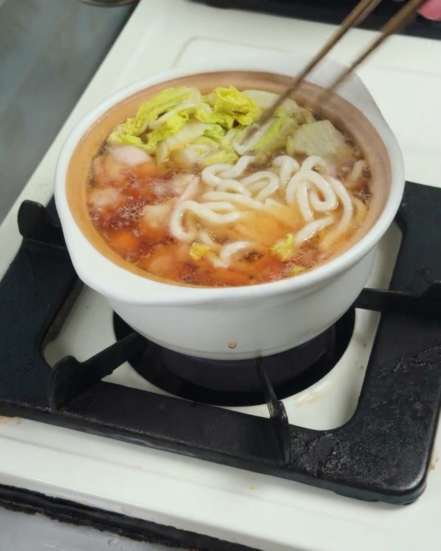 Añadiendo fideos udon a la olla con pollo, caldo y bok choy.