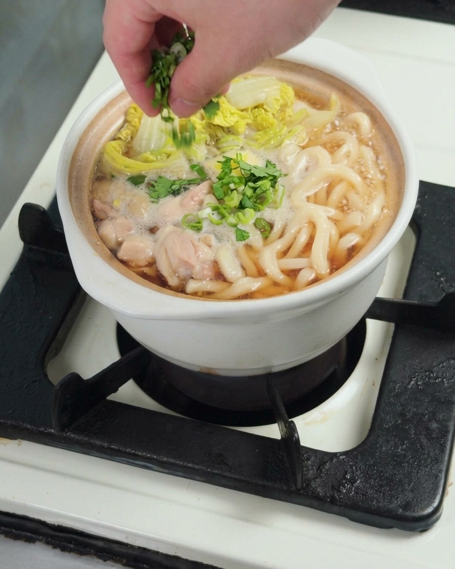 Espolvoreando cebolleta fresca picada sobre el tazón de udon con pollo.