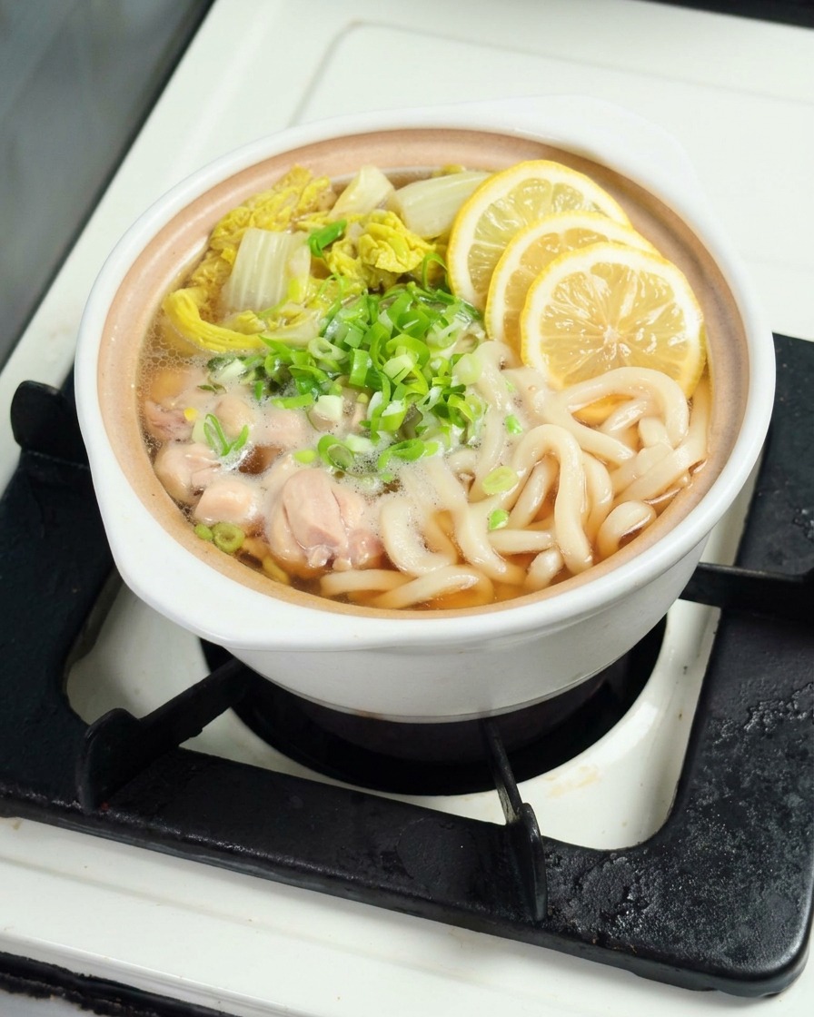 Rodajas finas de limón amarillo sobre la sopa de udon humeante.
