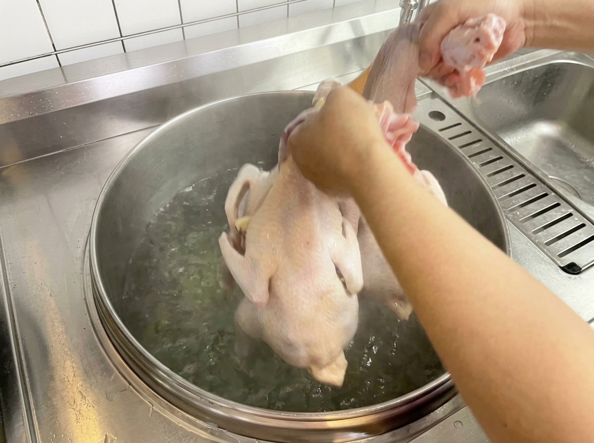 Un pollo crudo siendo sumergido en una olla grande con agua hirviendo.