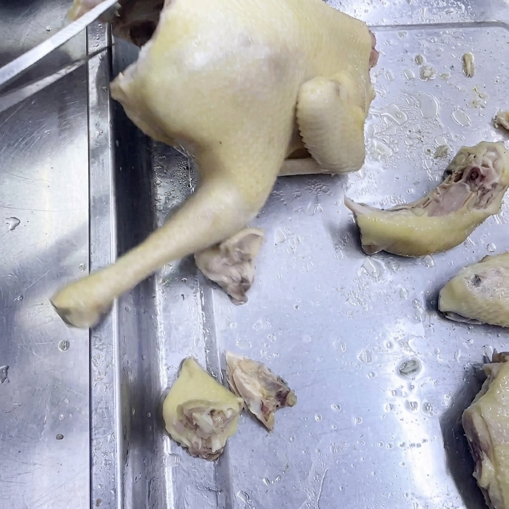 Unas tijeras de cocina cortando pollo cocido sobre una superficie de acero.