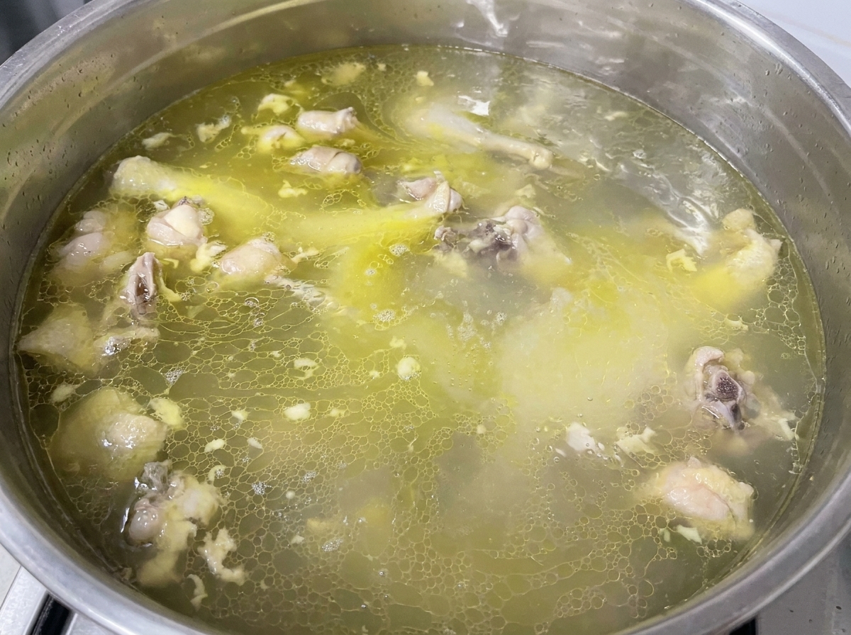 Condimentos siendo añadidos a una olla de caldo de pollo dorado hirviendo.