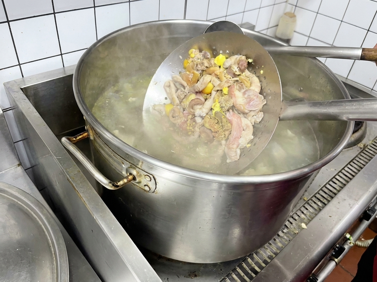 Menudencias de pollo siendo blanqueadas en un colador metálico sobre agua hirviendo.