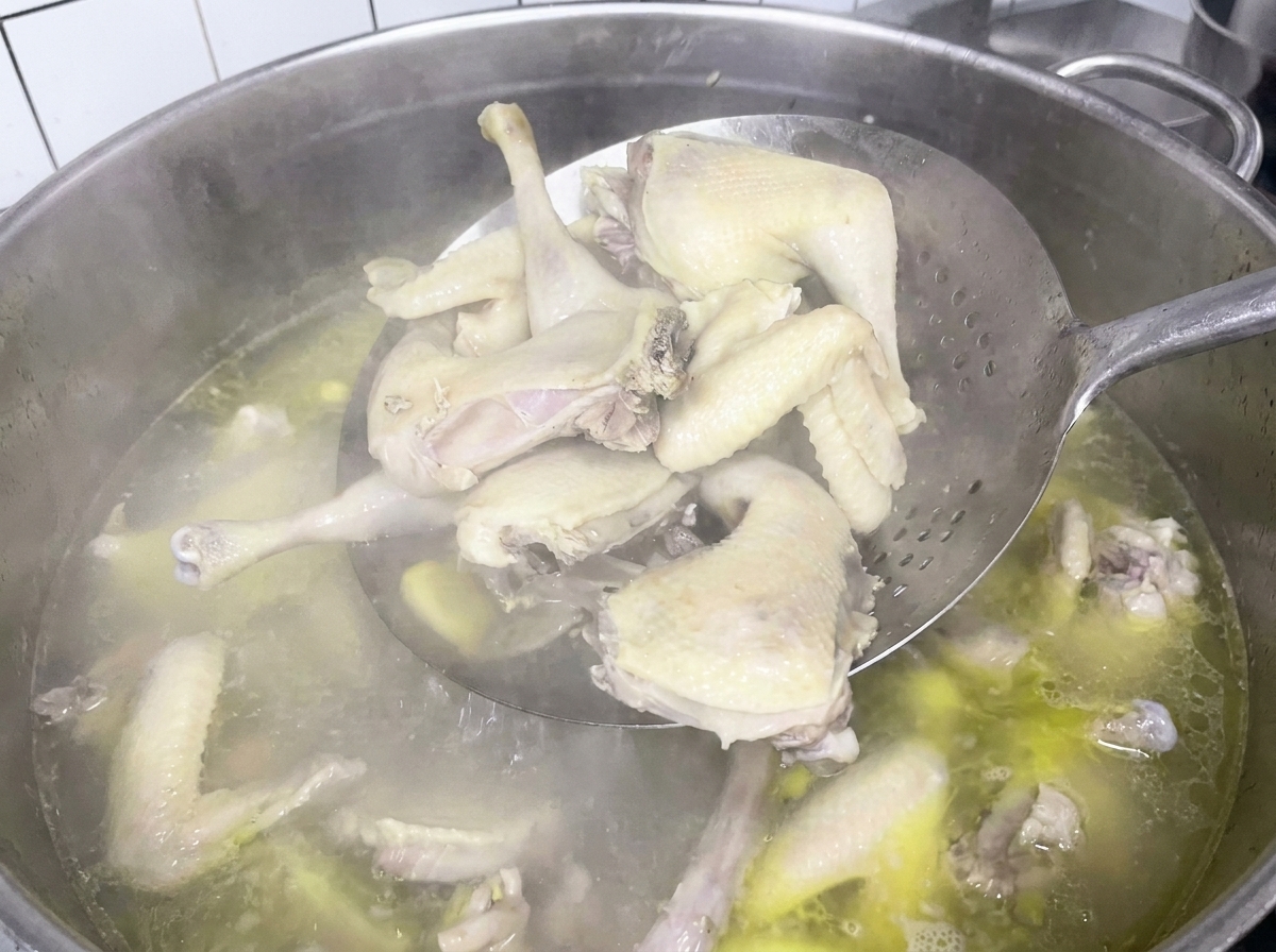 Trozos de pollo hervido siendo retirados de la olla con una espumadera.