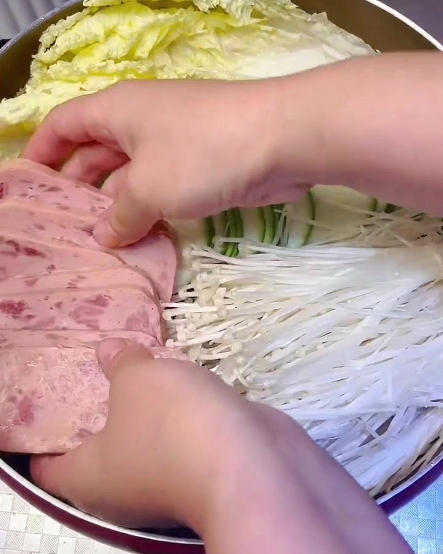 Carne en conserva en rodajas y setas enoki siendo organizadas sistemáticamente en la olla.