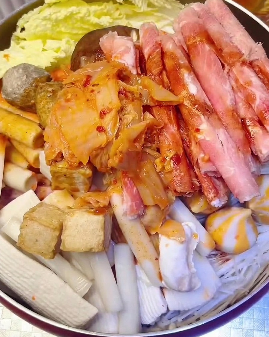 Un montón de kimchi rojo picado siendo añadido a la olla mientras se vierte agua.