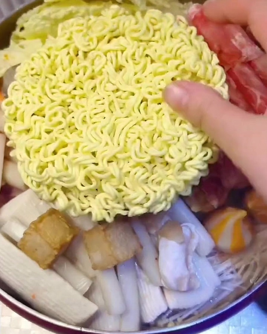 Un bloque de fideos instantáneos cubierto con lonchas de queso amarillo siendo colocado en la olla.