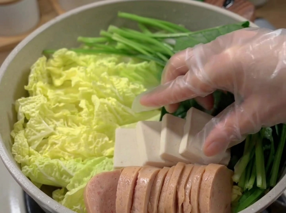 Una olla ancha llena con capas de carne, tofu, pasteles de pescado y vegetales.