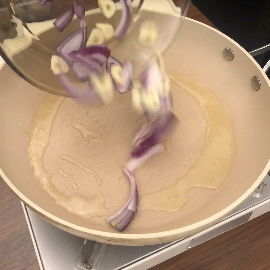 Almejas frescas, cebolla picada y ajo vertiéndose en una sartén con aceite caliente.