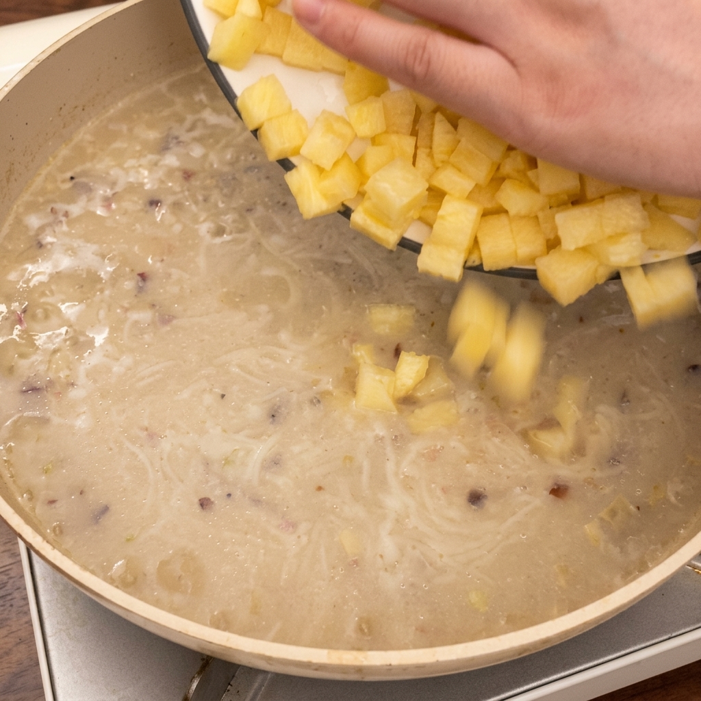 Mano dejando caer cubos de papa en la sartén con la sopa hirviendo a fuego lento.