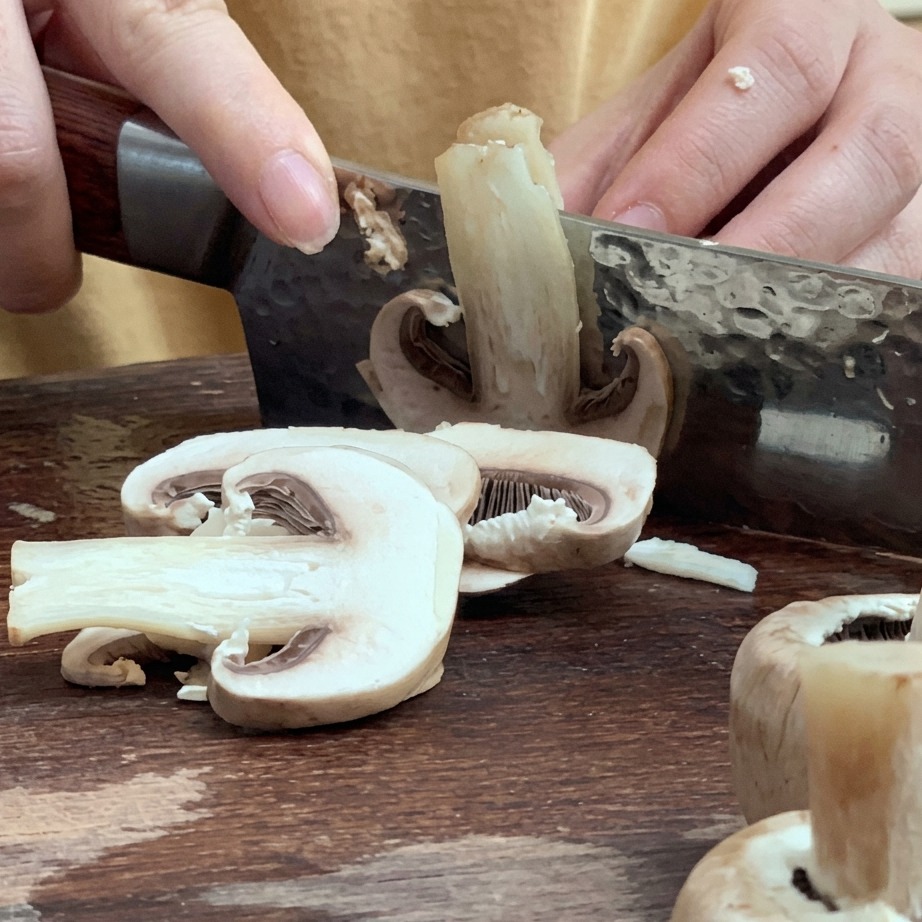 Champiñones frescos siendo cortados en láminas finas sobre una tabla de madera.