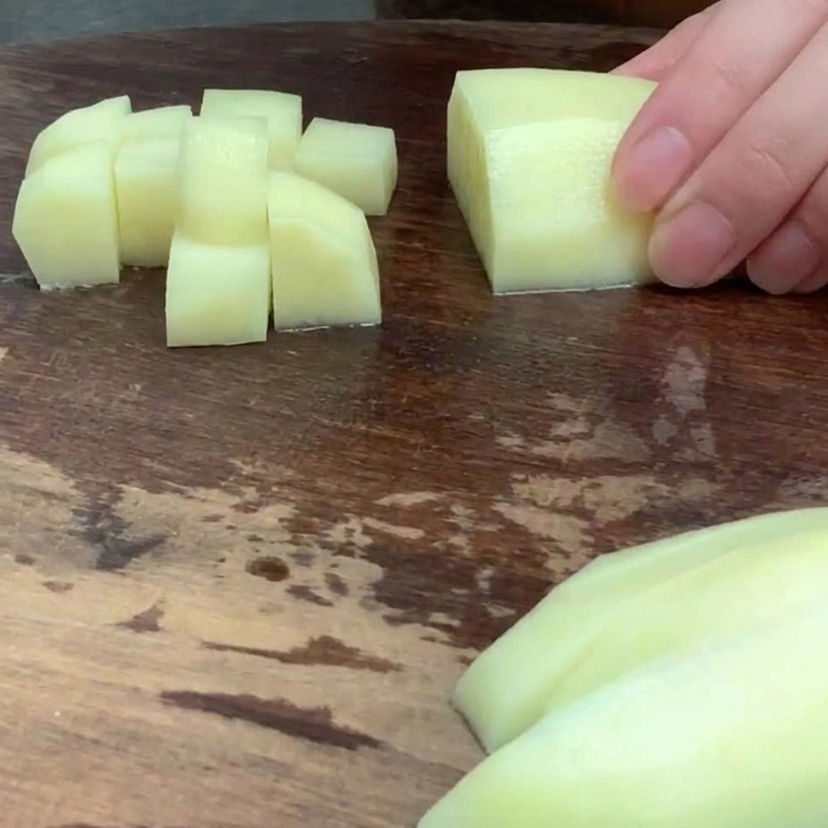 Papa pelada cortada en cubos pequeños y uniformes sobre una tabla de madera.