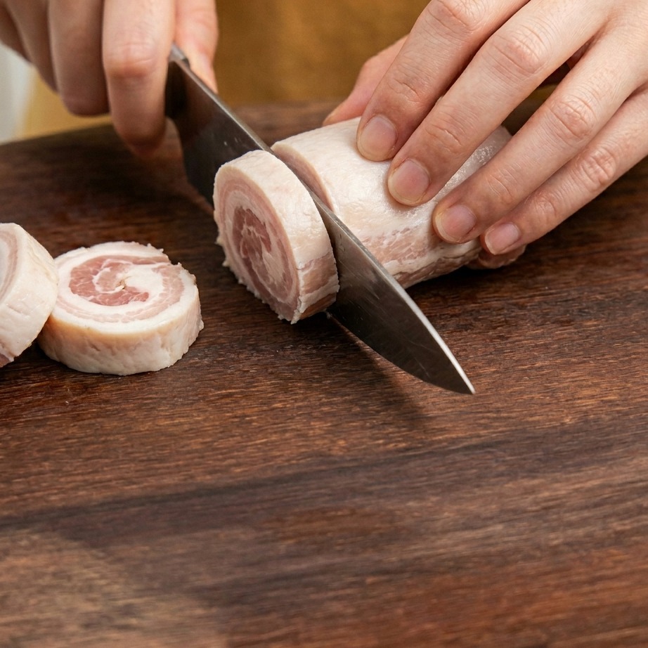 Rebanadas de tocino siendo cortadas en trozos pequeños sobre una tabla de madera.