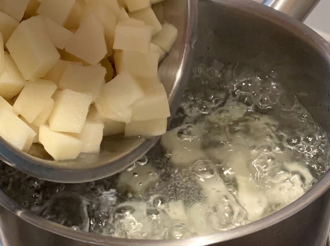 Cubos de papa hirviendo en una olla de agua en la estufa.