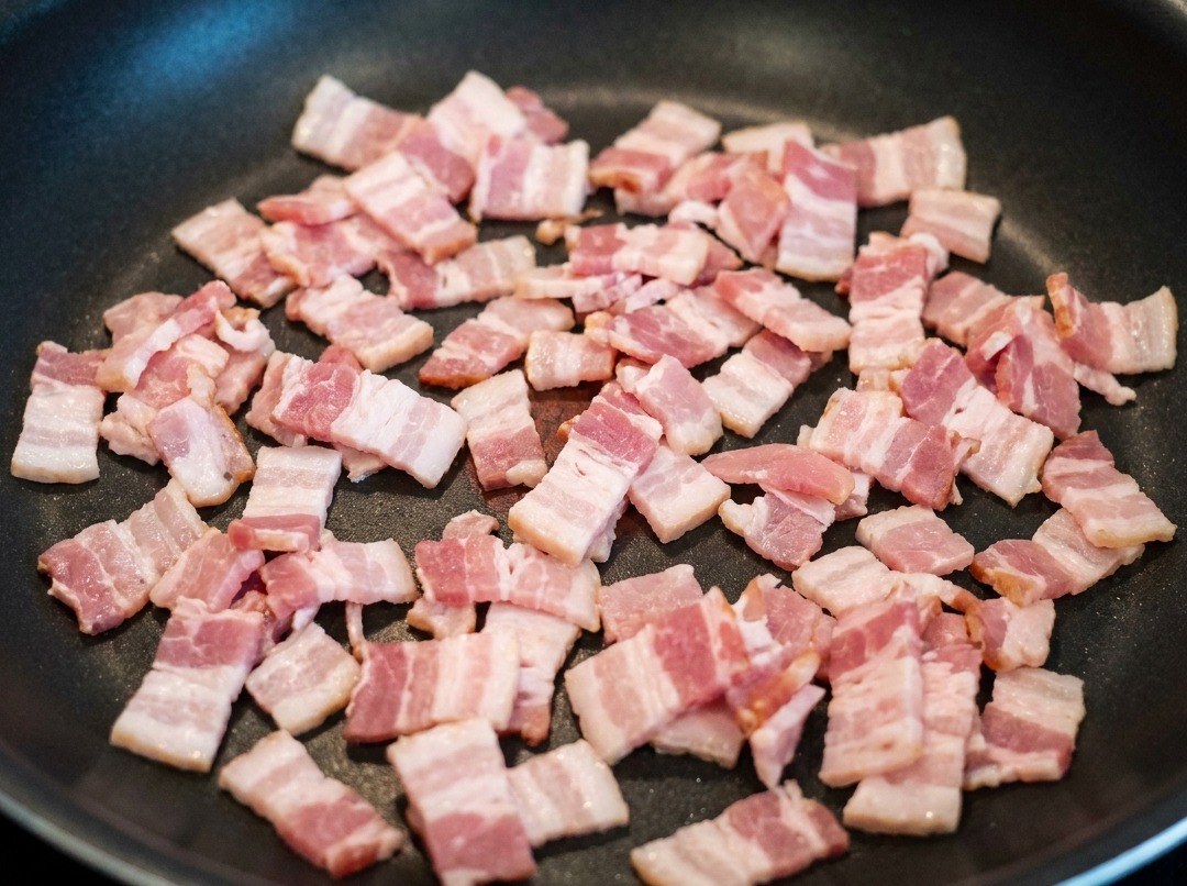 Trozos de tocino friéndose en un sartén, soltando su grasa sabrosa.