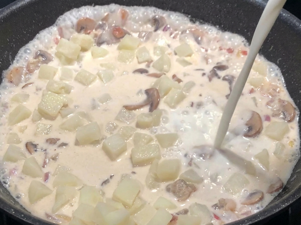 Leche siendo añadida al sartén hasta cubrir los ingredientes, mientras la mezcla hierve suavemente.