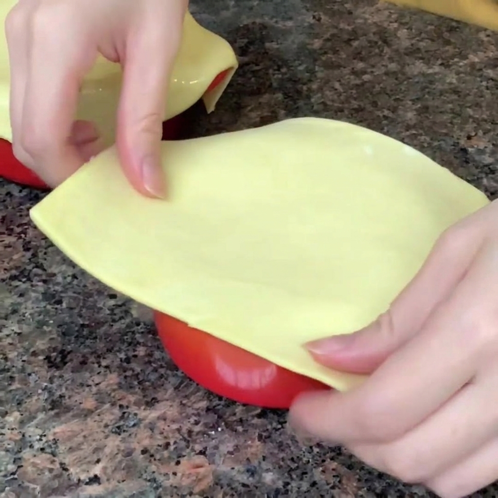 Una hoja de hojaldre siendo colocada y sellada sobre el borde de un tazón con sopa.