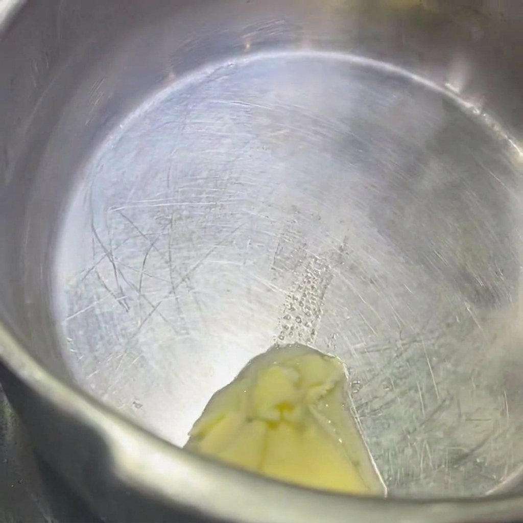 Un primer plano de un trozo de mantequilla derritiéndose en una olla de acero inoxidable.