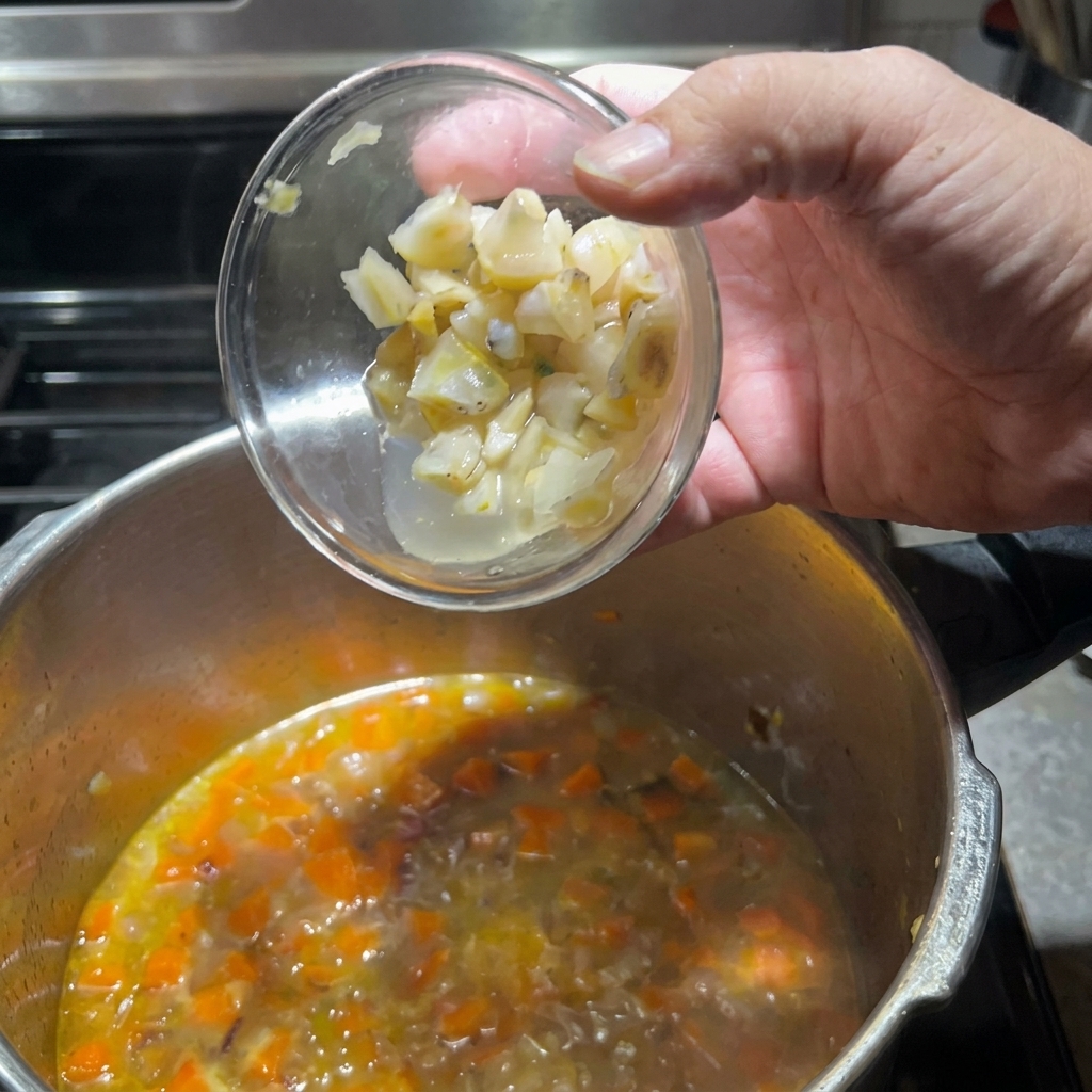 Añadiendo los trozos de almeja preparados a la olla con verduras.