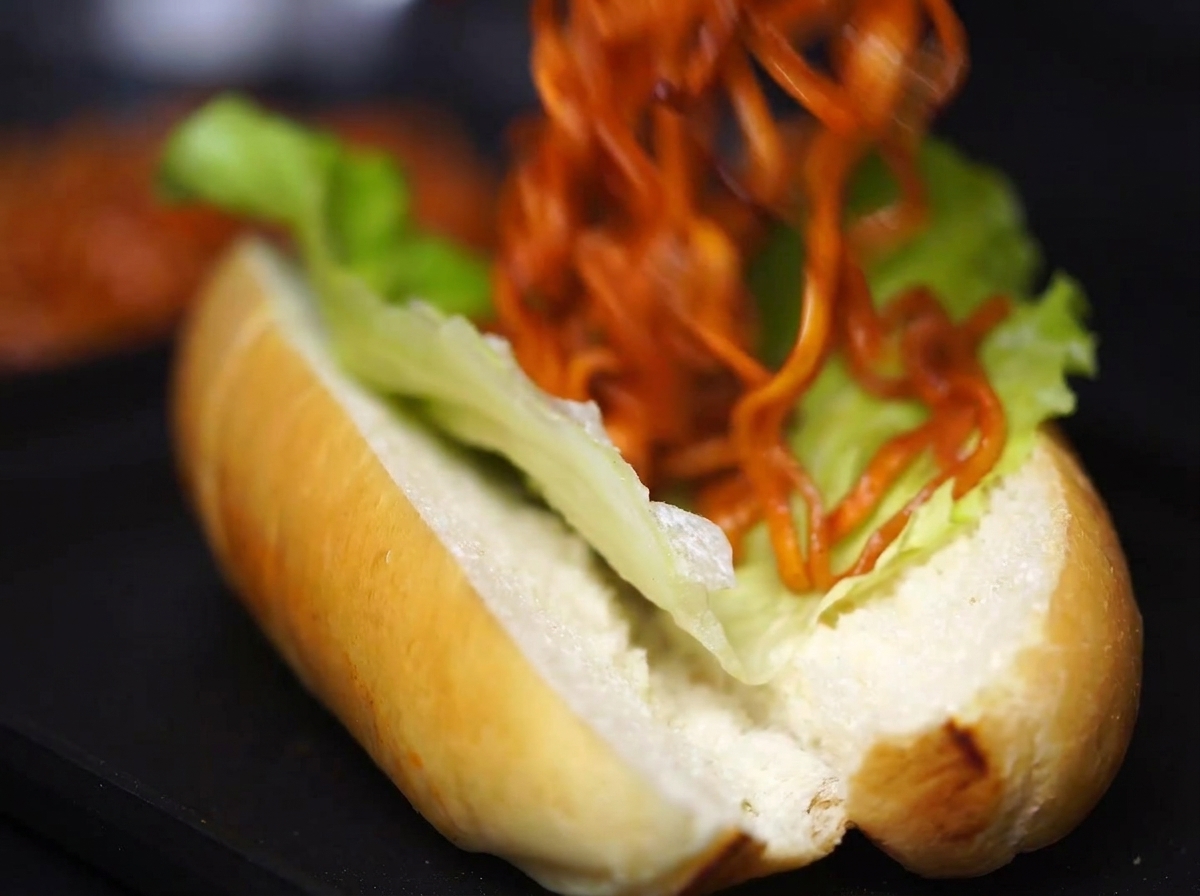 Una gran porción de fideos cocidos con salsa siendo colocados cuidadosamente dentro del pan con lechuga.