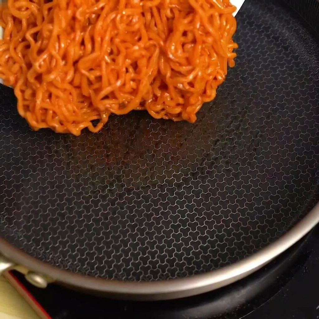 Fideos picantes siendo vertidos desde un tazón en una sartén negra caliente.