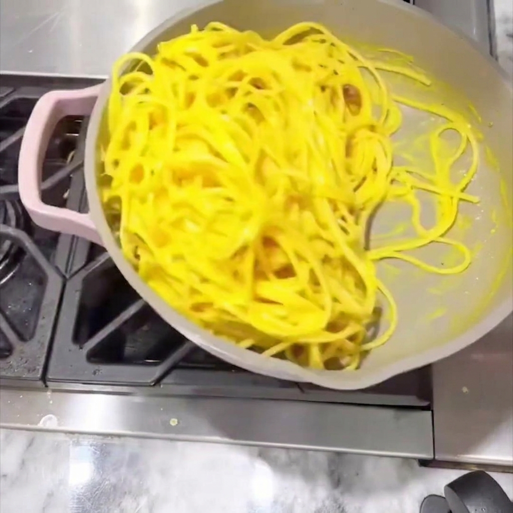 Espaguetis removidos en la sartén con una salsa cremosa hasta quedar cubiertos.