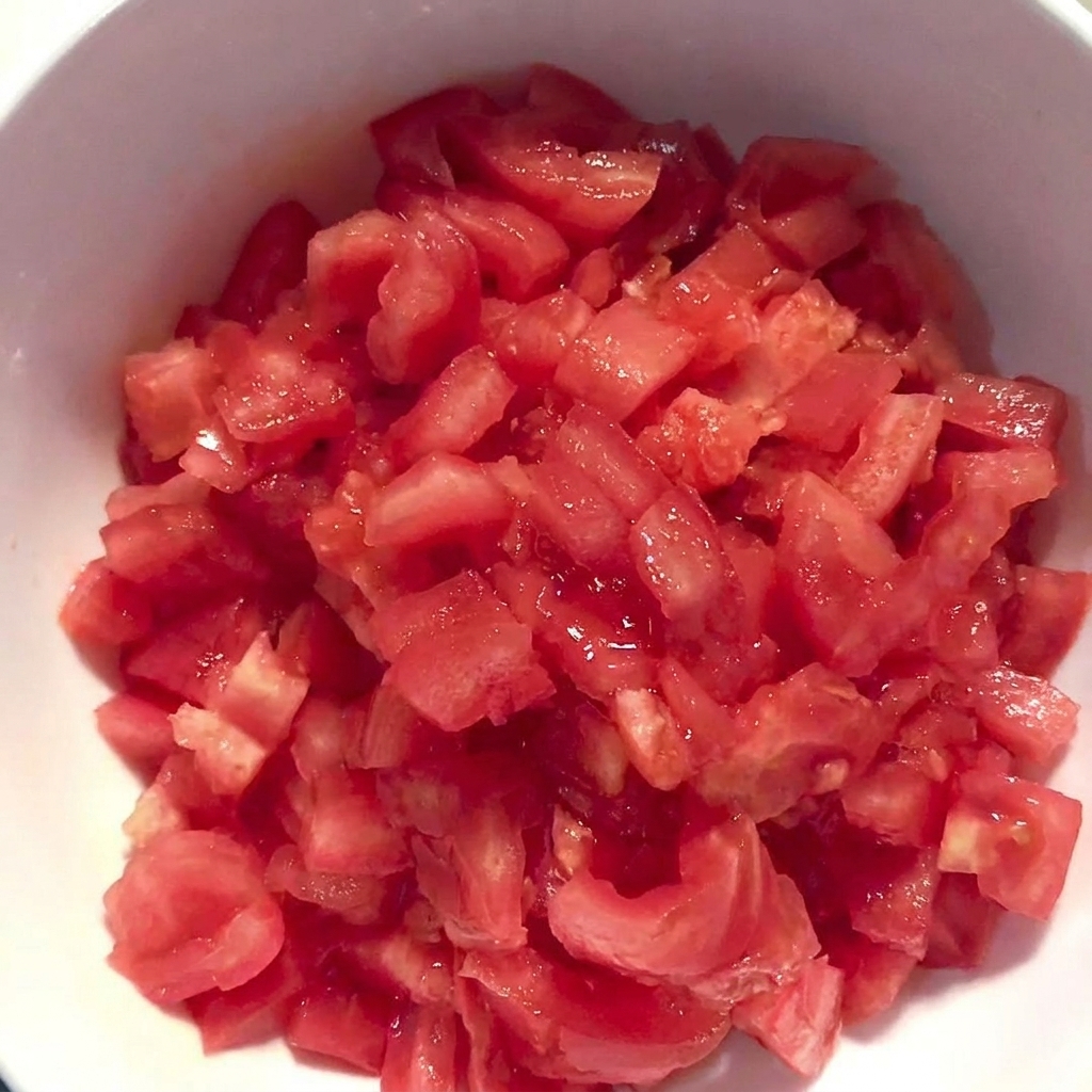 Un tazón blanco lleno de tomates frescos pelados y cortados en cubitos.