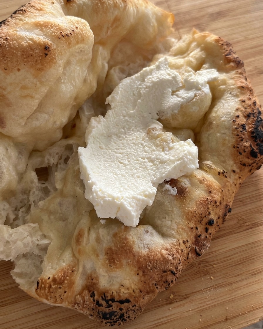 Una capa gruesa de queso ricotta blanco colocada dentro del pan de pizza recién horneado y abierto.