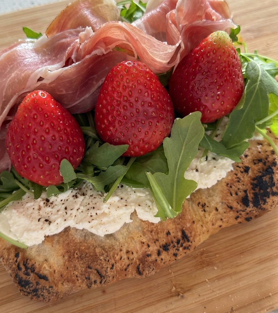 Un primer plano de rebanadas de prosciutto dobladas sobre fresas frescas y rúcula.