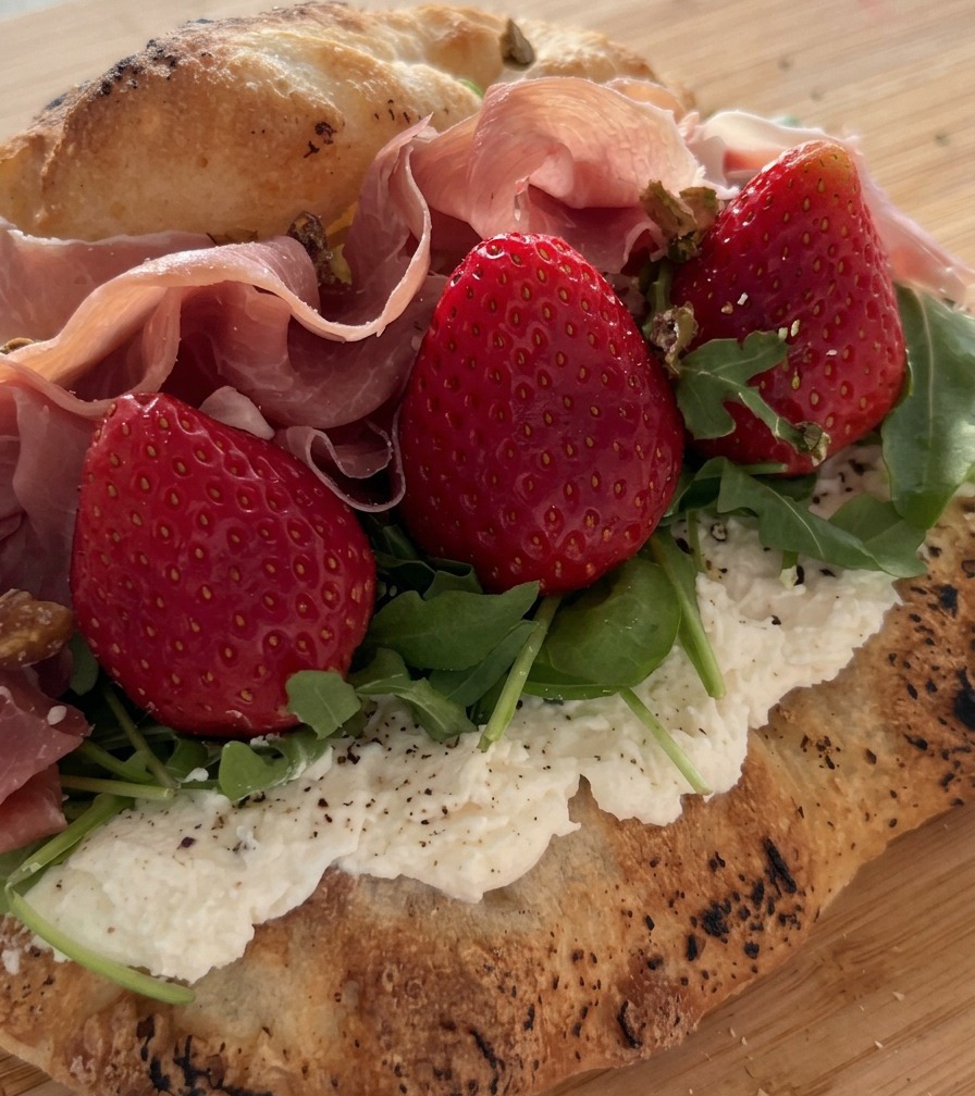 Pistachos triturados esparcidos sobre un sándwich relleno de prosciutto, fresas y rúcula.