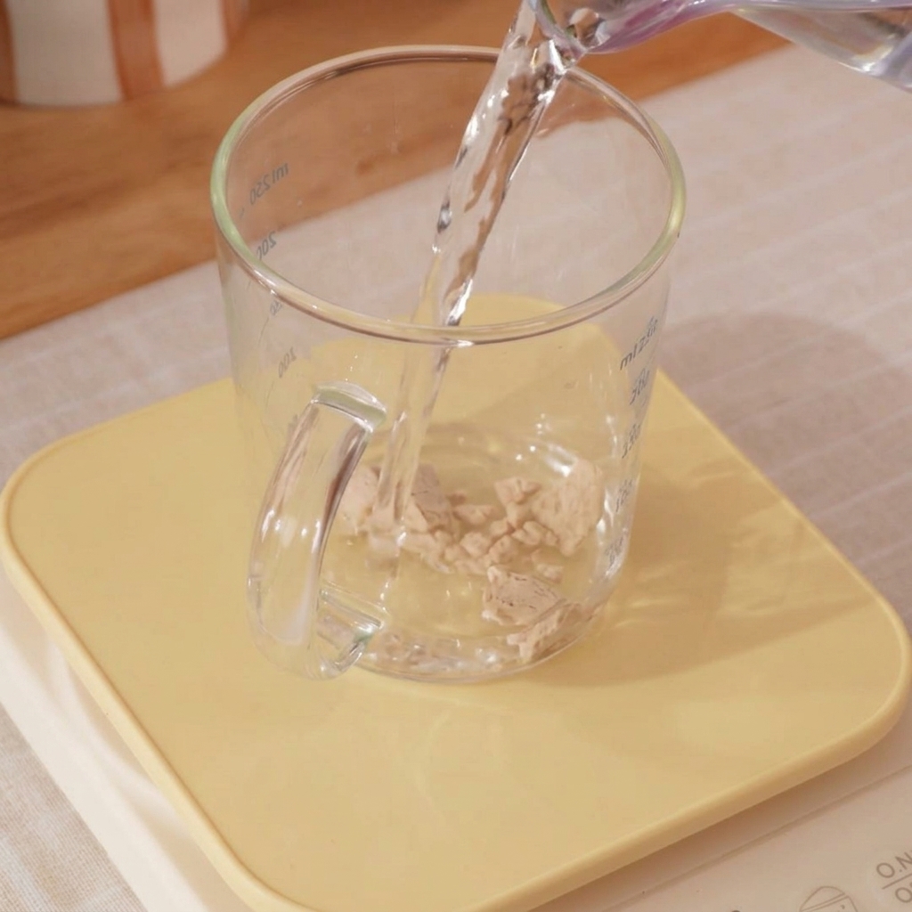 Primer plano de una taza con agua helada y levadura siendo mezclada con un pequeño batidor.