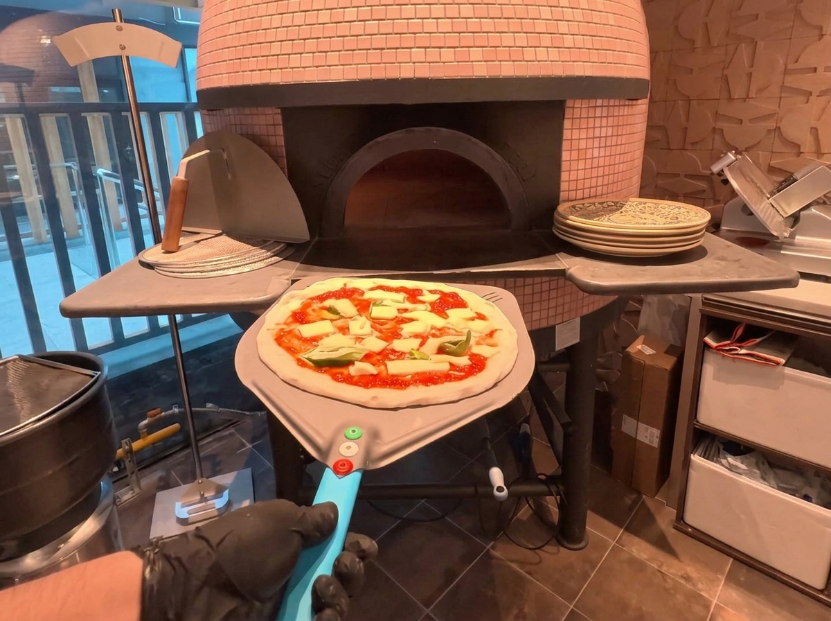 Una pizza en una pala de metal siendo introducida en un horno de leña tradicional.