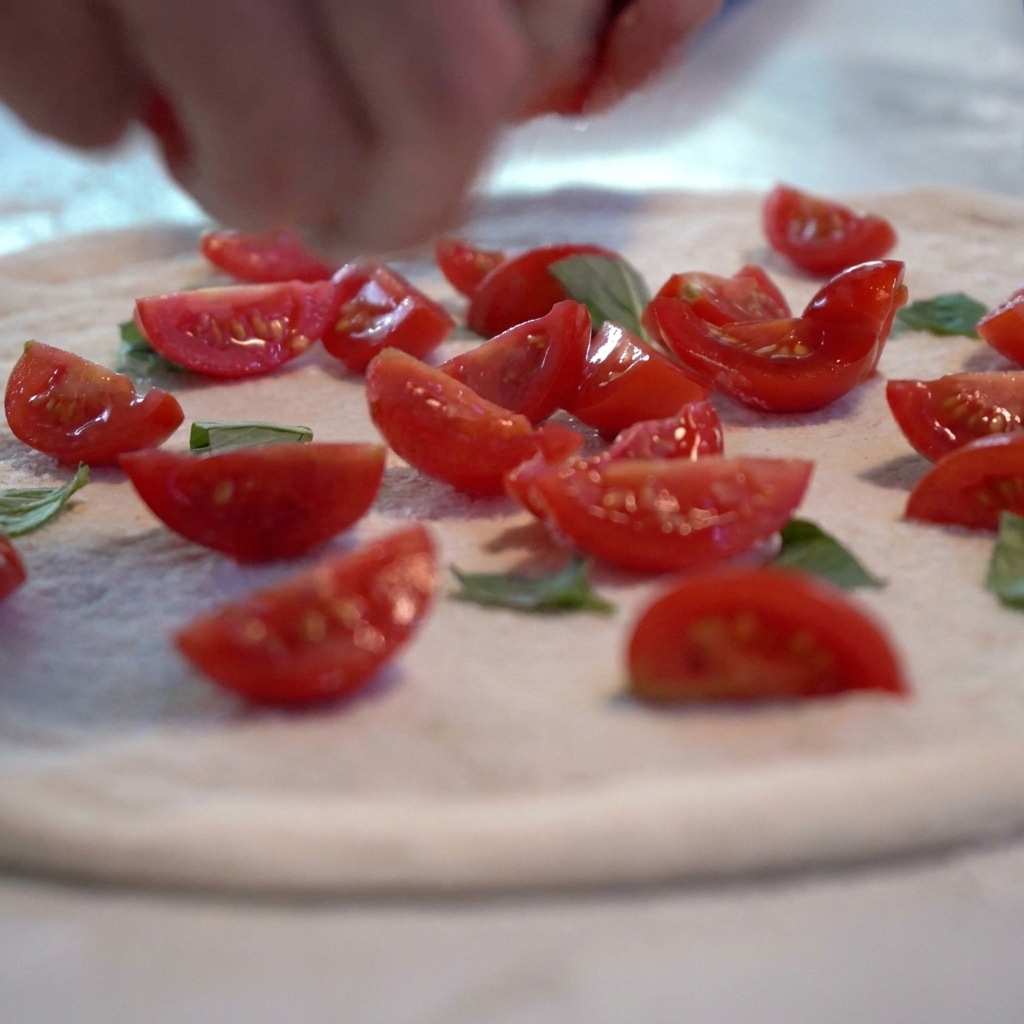 Salsa de tomate y rodajas de tomate fresco siendo añadidas a la base de masa cruda.