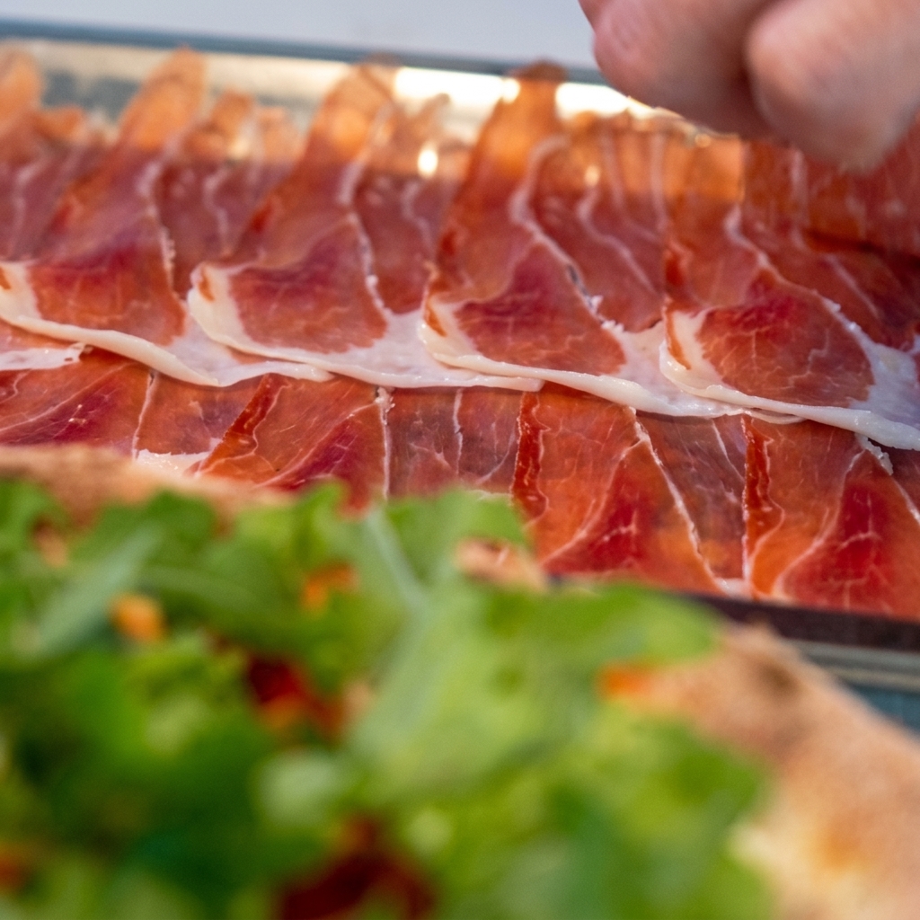 Lonchas finas de prosciutto dispuestas cuidadosamente sobre la pizza cubierta de rúcula.