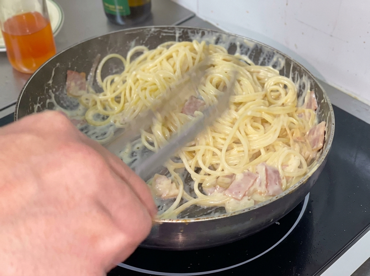 Una porción de espaguetis cocidos siendo colocados en la salsa cremosa dentro de la sartén.