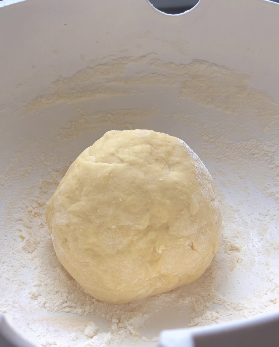 Una bola lisa y redonda de masa cruda amasada reposando en el centro de un tazón blanco.