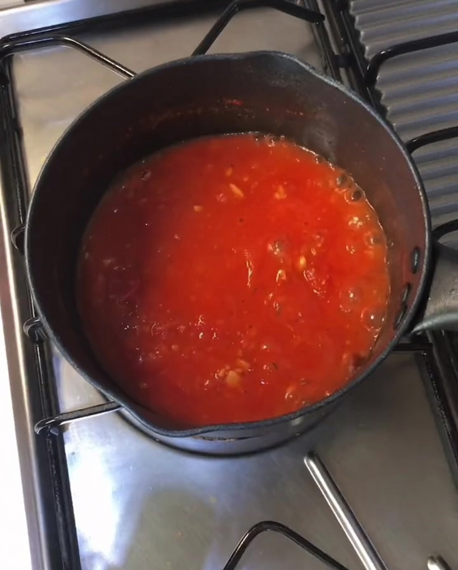 Salsa de tomate roja espesa y burbujeante cocinándose a fuego lento en una olla negra sobre una estufa.