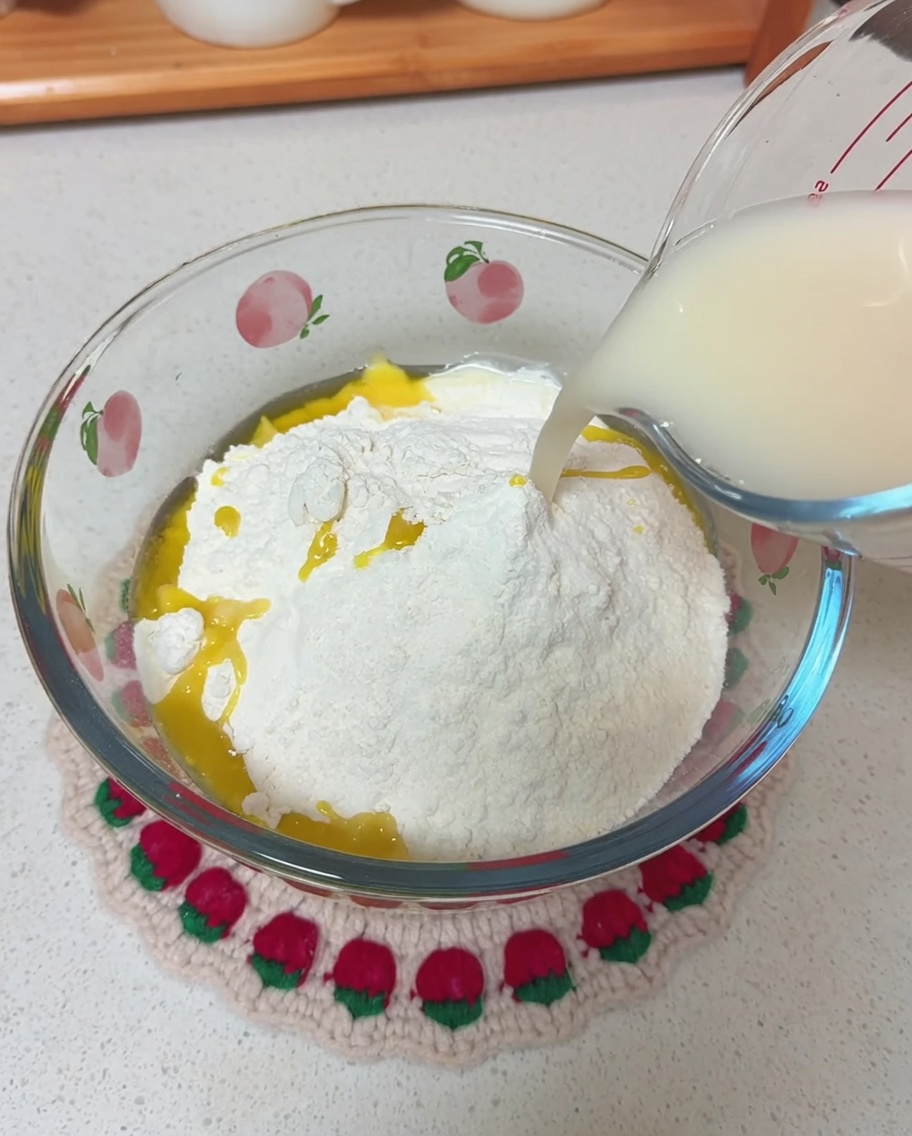 Vertiendo una mezcla lechosa de agua y levadura desde una taza medidora a un bol con harina seca y aceite de oliva.