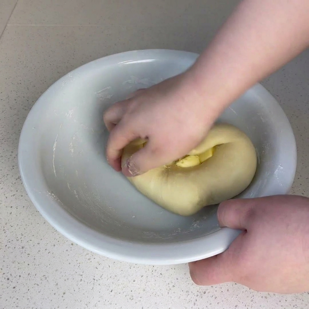 Manos integrando la mantequilla en la masa dentro del bol.
