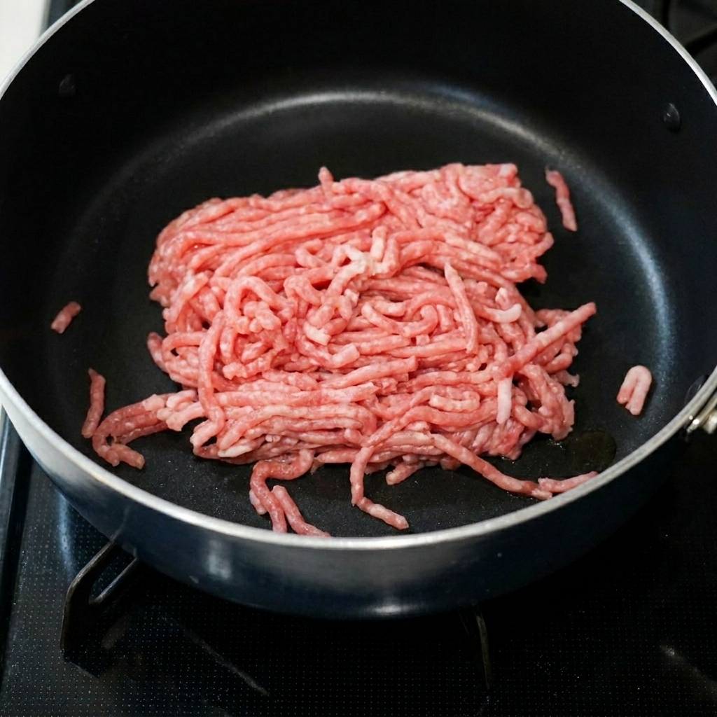 Carne picada de cerdo cocinándose en una sartén con pasta de frijoles picante y ajo.