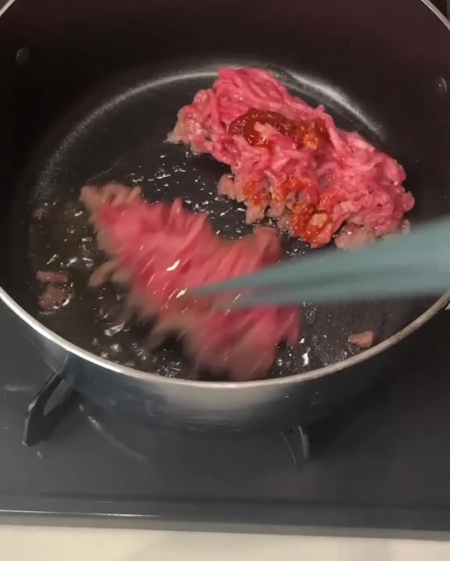 Palillos levantando y removiendo trozos de carne picada de cerdo cubiertos de una pasta de chile rojiza dentro de una olla.