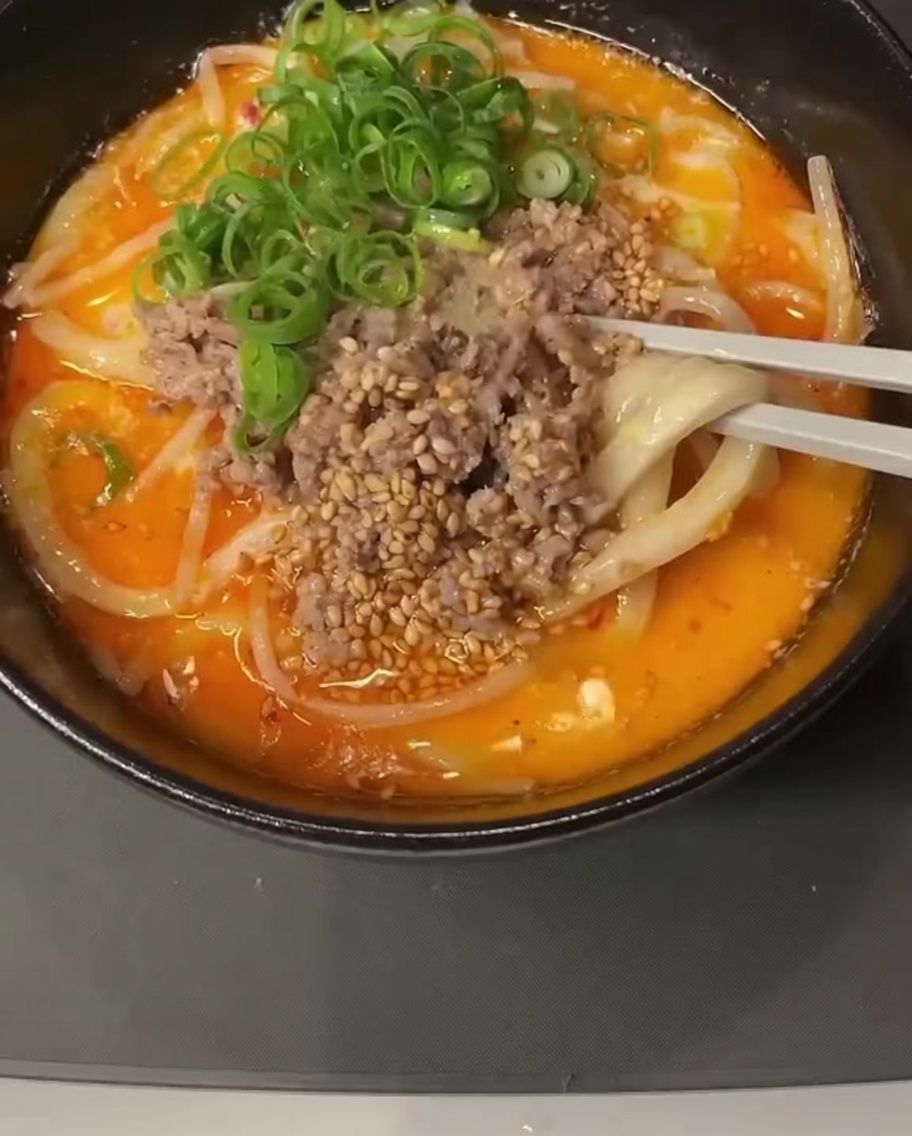 Un primer plano de una olla que contiene una mezcla líquida cremosa a la que se le añade y remueve una cucharada de pasta de miso.