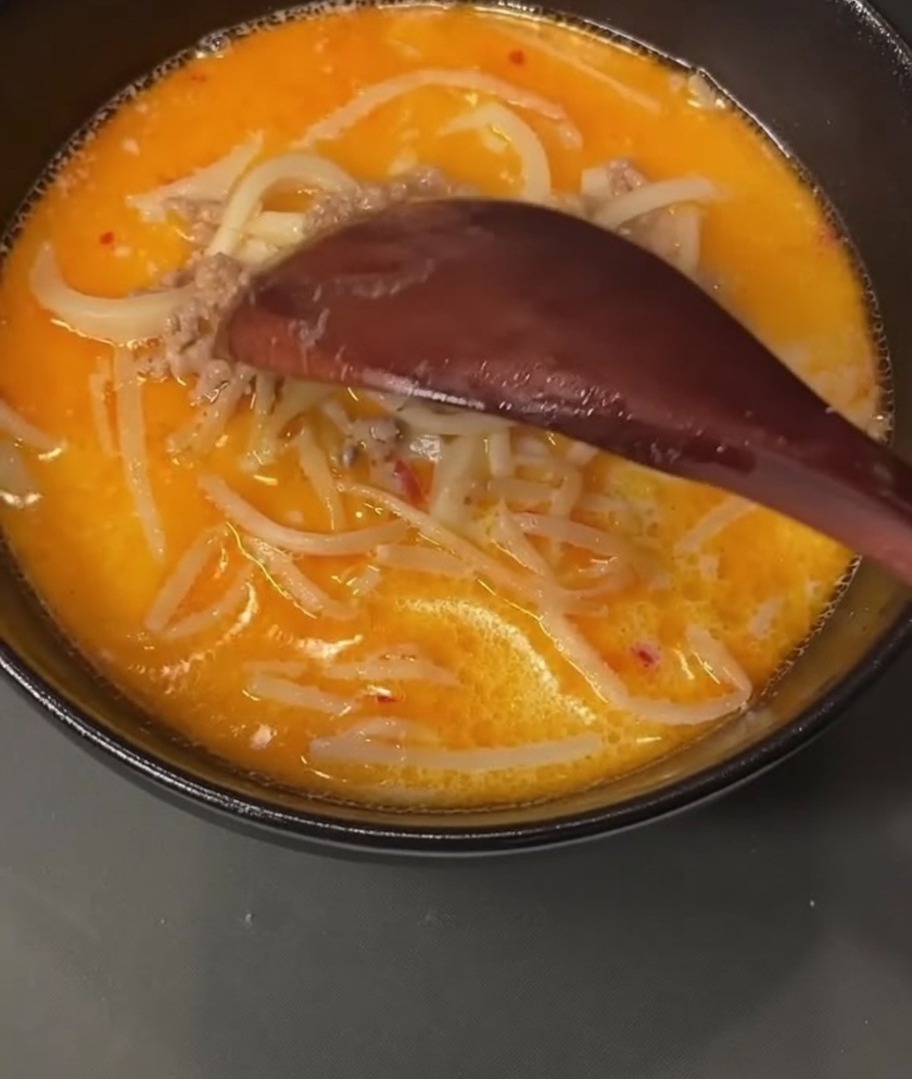 Una cuchara de madera recogiendo carne picada de cerdo cocinada de una olla llena de caldo.