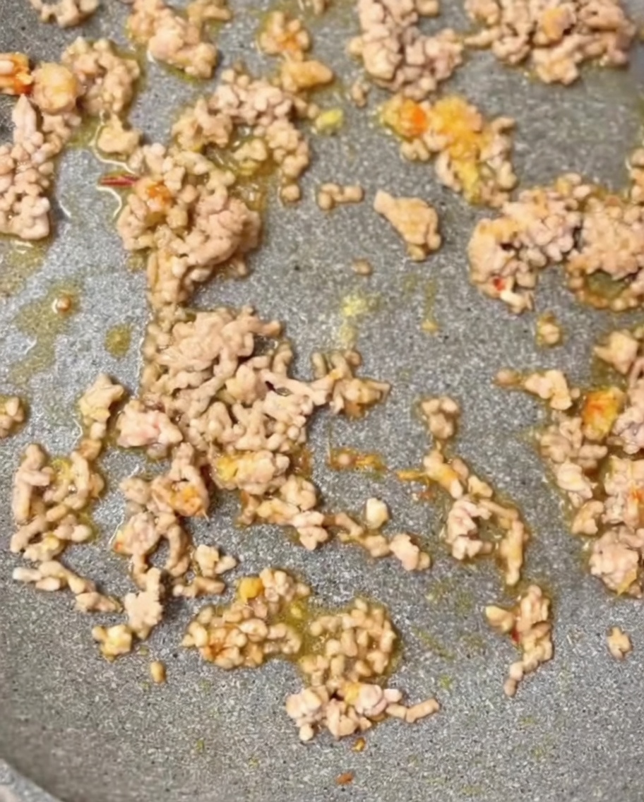 Condimentos incluyendo sésamo molido y caldo de pollo añadidos a la sartén.