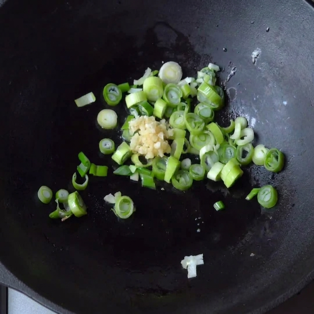 Ajo picado siendo añadido al wok con las cebollas verdes.