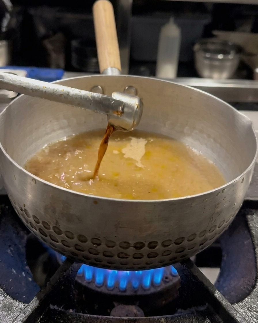 Salsa de soja vertiéndose en la olla con caldo y mezclándose con un batidor.